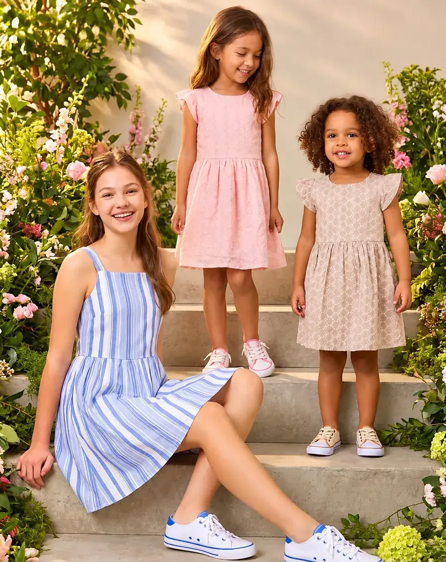 Três meninas de idades diferentes com vestidos de verão sentadas e em pé numa escada com flores