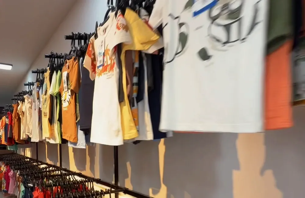 Parede da loja com camisetas infantis penduradas em araras